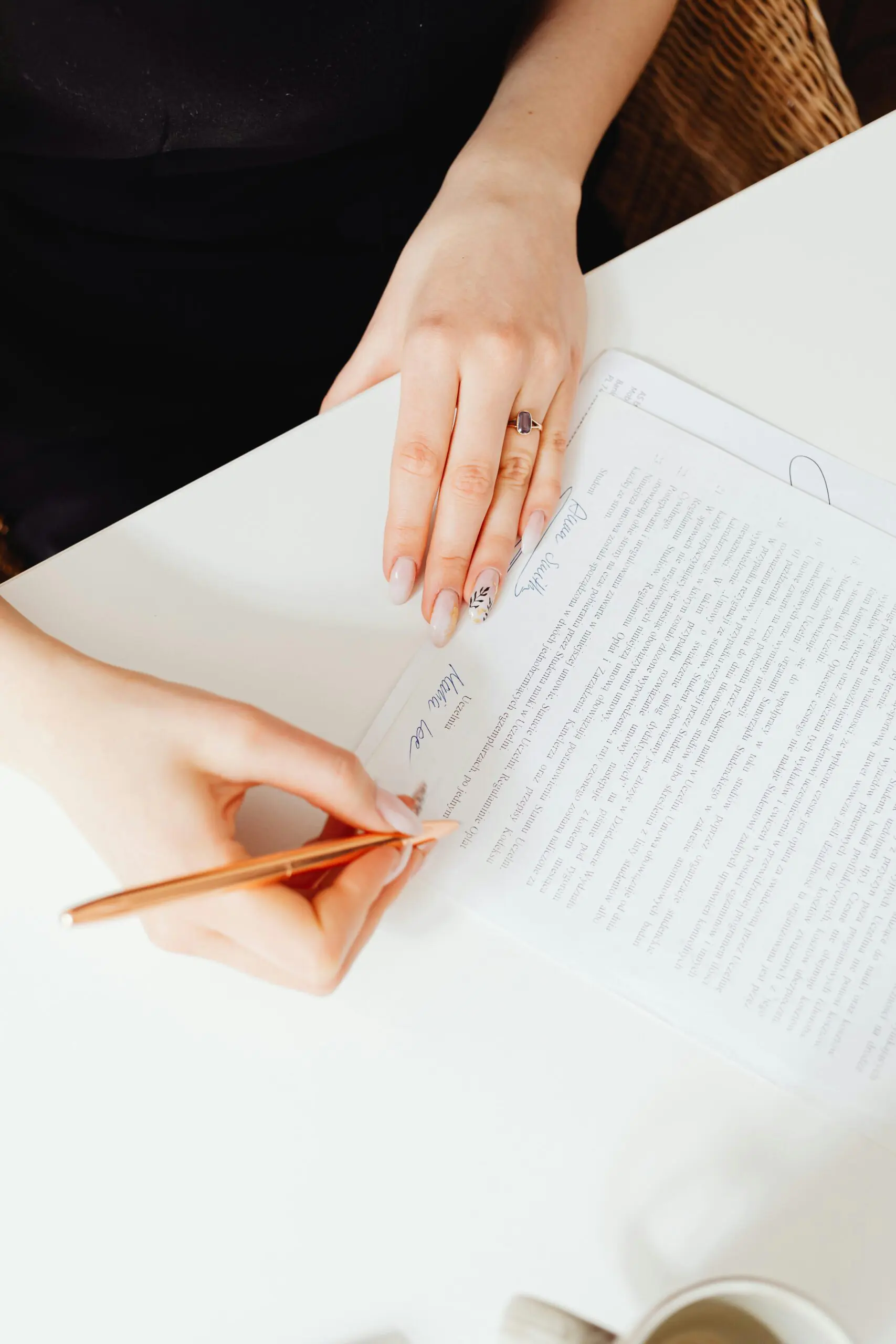 A woman's hands holding a pen over a paper document. Indoor writing scene.
